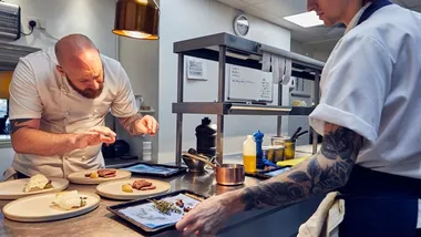 A chef puts the finishing touches to a dish while another chef looks on 