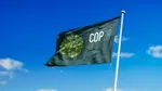 A green flag bearing the logo for COP 28 flutters in a clear blue sky.