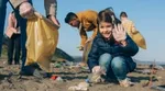 A young girl holding a rubbish bag, waving as she collects rubbish off a beach